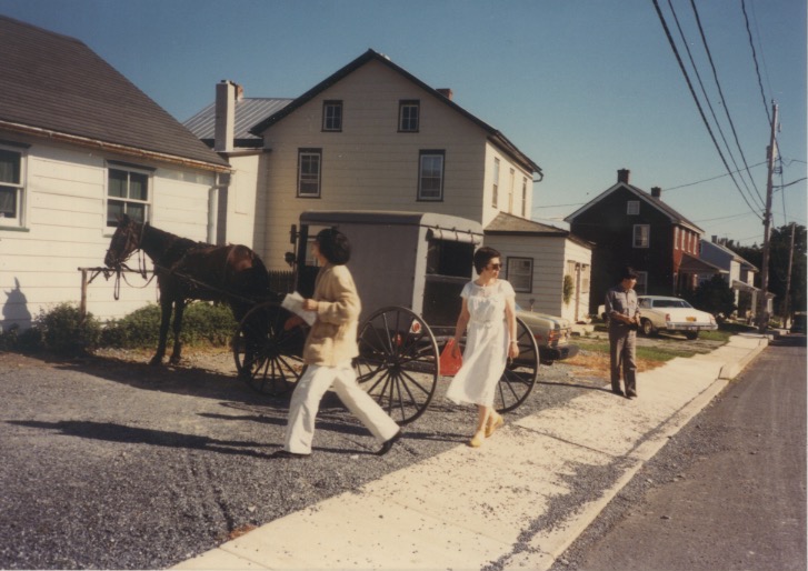 Madeline and Arakawa walking on a street near a horse drawn trailer (Sep 1986)